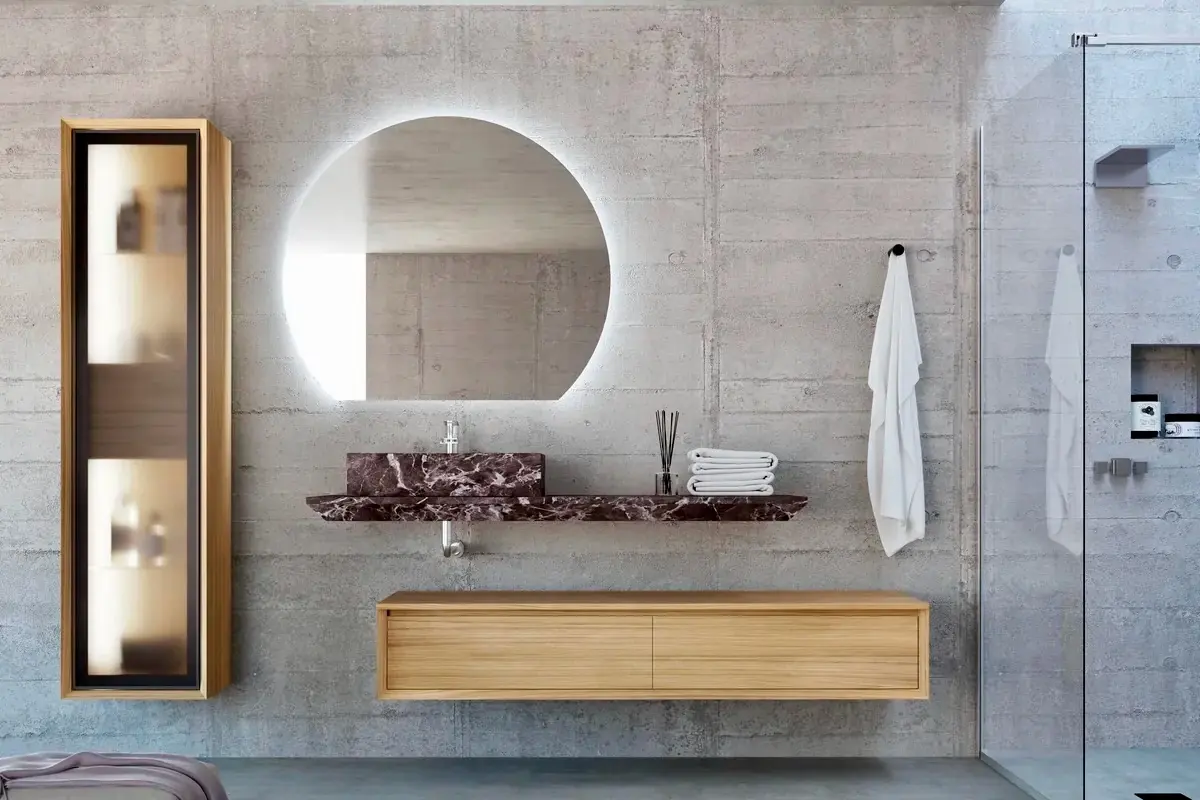 Baño de hormigón con mueble de madera a medida de AD Bath, encimera de mármol rojo, espejo con luz y columna con vitrina