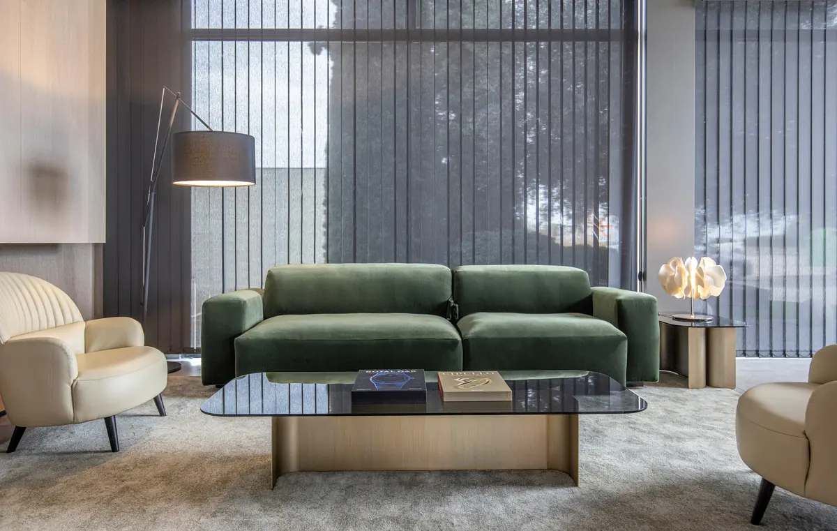 Salón de Colección Alexandra con sofá de terciopelo verde, butacas claras y mesa baja de cristal frente a un ventanal