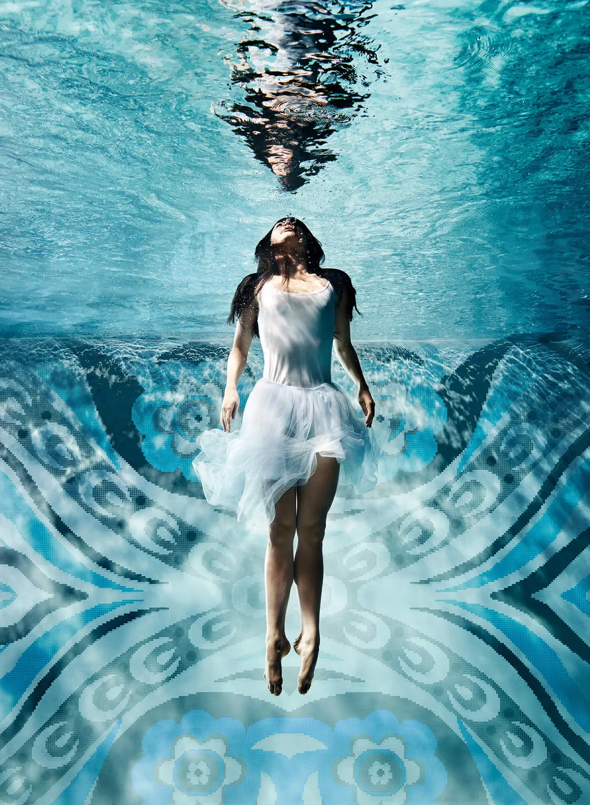 Mujer vestida de blanco sumergida en una piscina con el fondo de mosaico Bisazza en azules y blancos