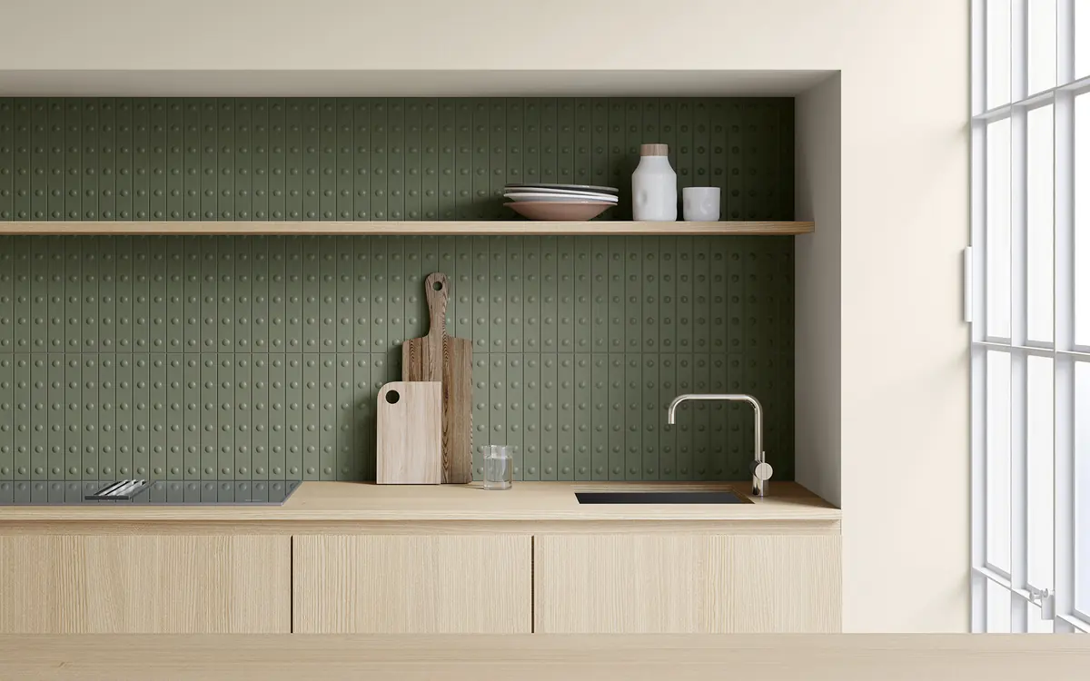 Cocina con la pared revestida de azulejos Mutina en verde salvia con relieve, sobre muebles y encimera de madera clara